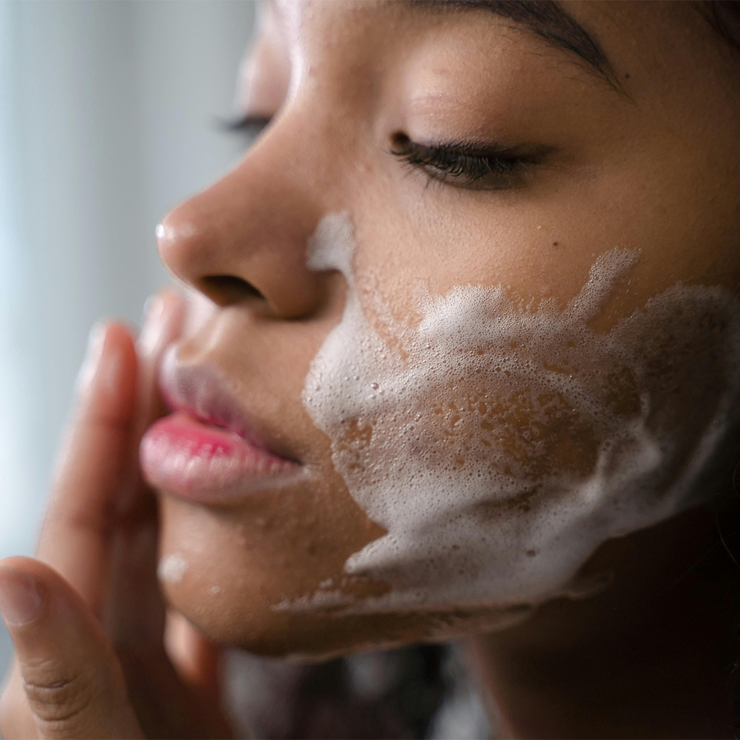 A young woman cleansing her cheek with a natural soap, showing a close-up of her face and smooth, healthy skin.