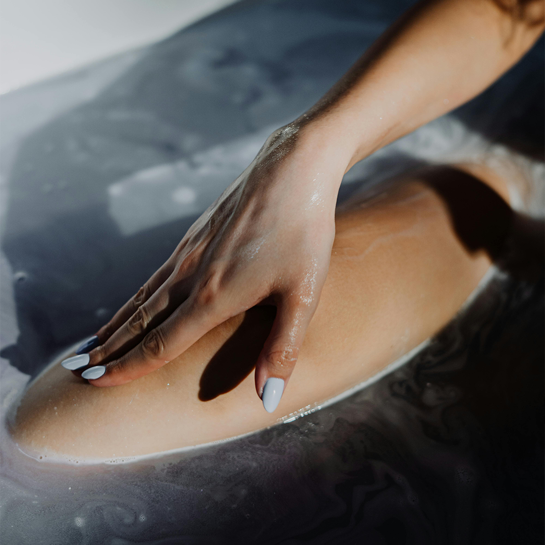 A close-up of a person’s hand gently resting on a knee, nourishing her skin and treating herself to a relaxing bath.